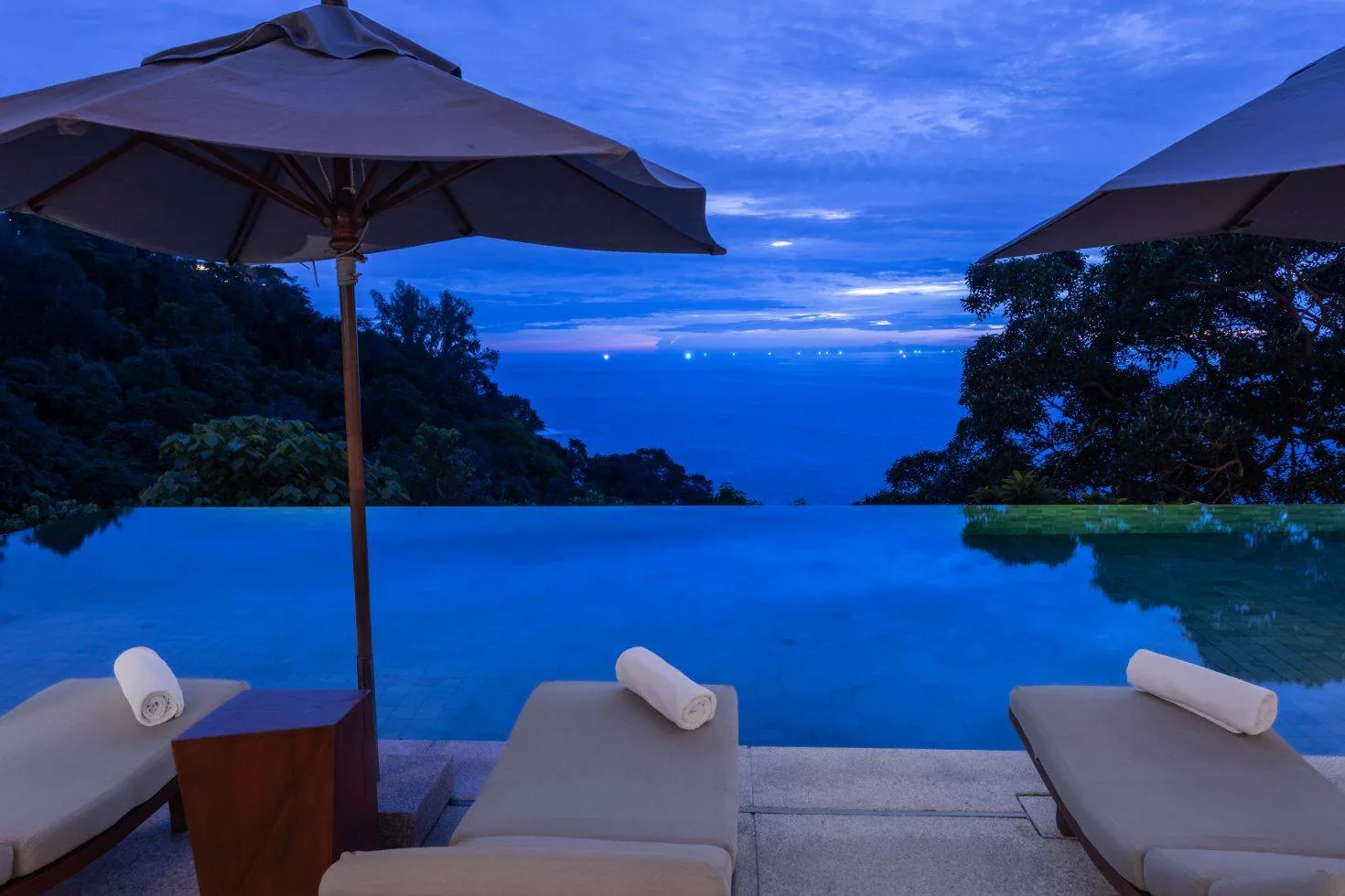 Sun loungers under umbrellas beside an infinity pool at dusk
