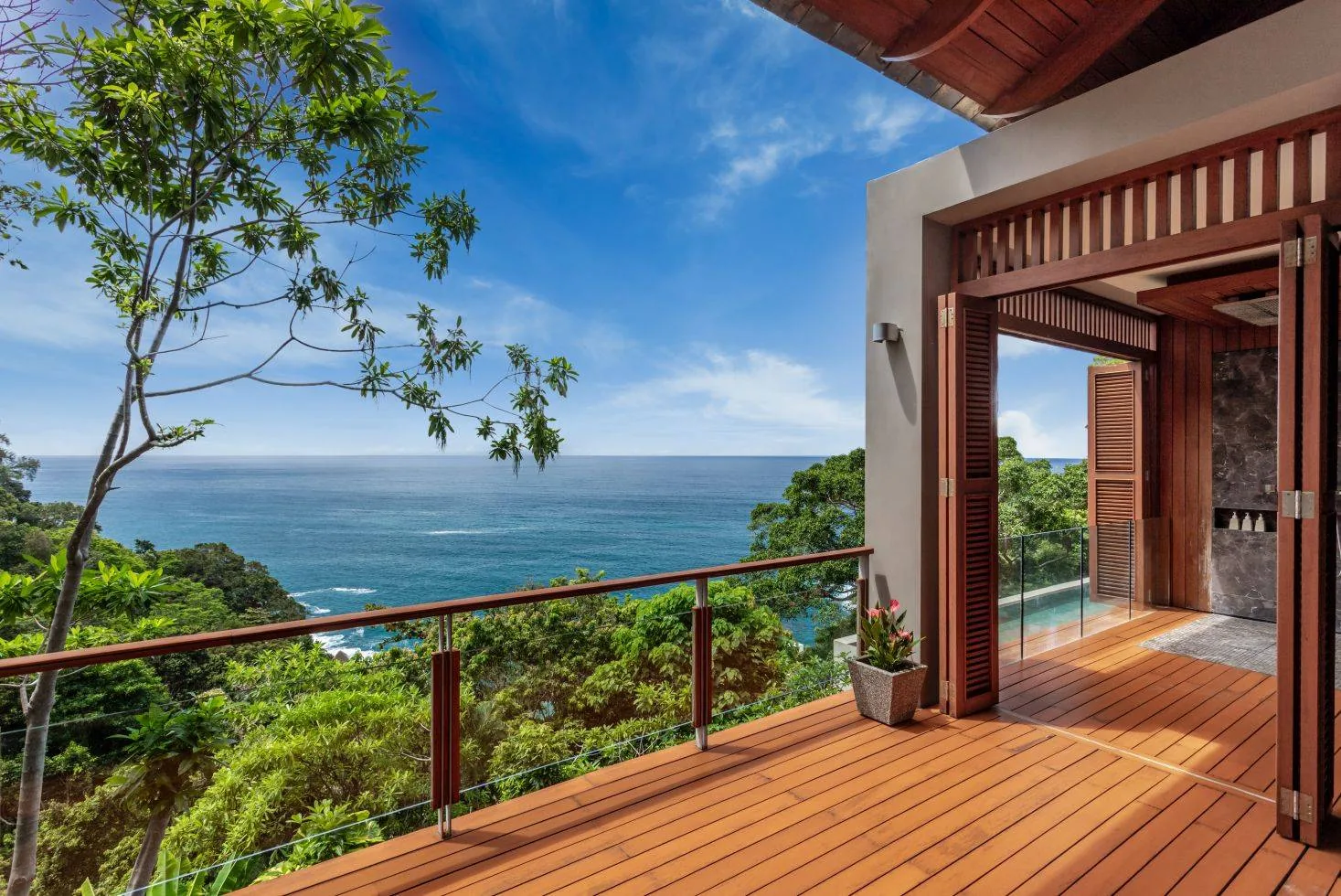 A timber deck with open doors leading to a room, overlooking the ocean