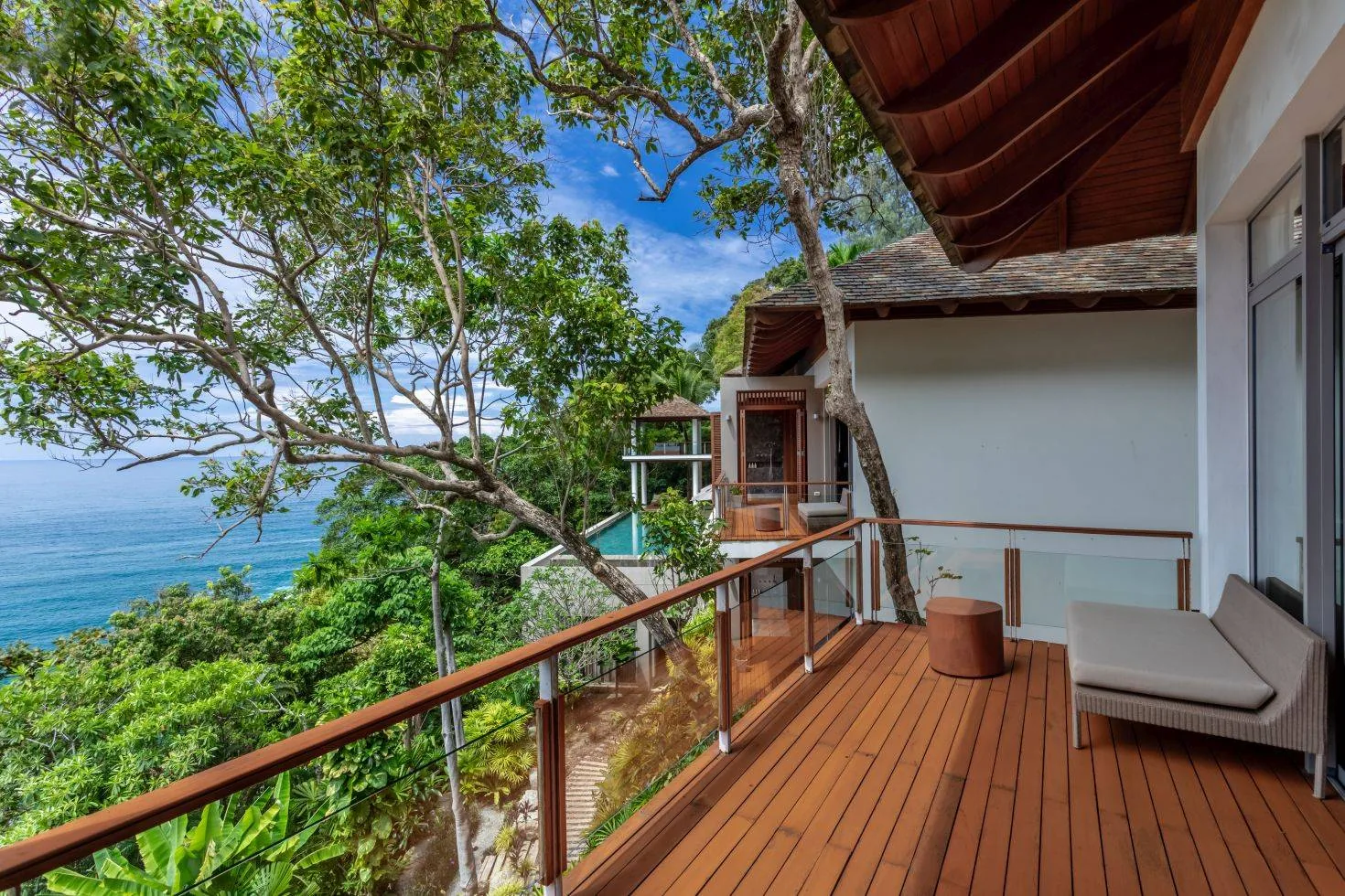 A timber deck walkway through trees with a glimpse of the ocean and another part of the villa
