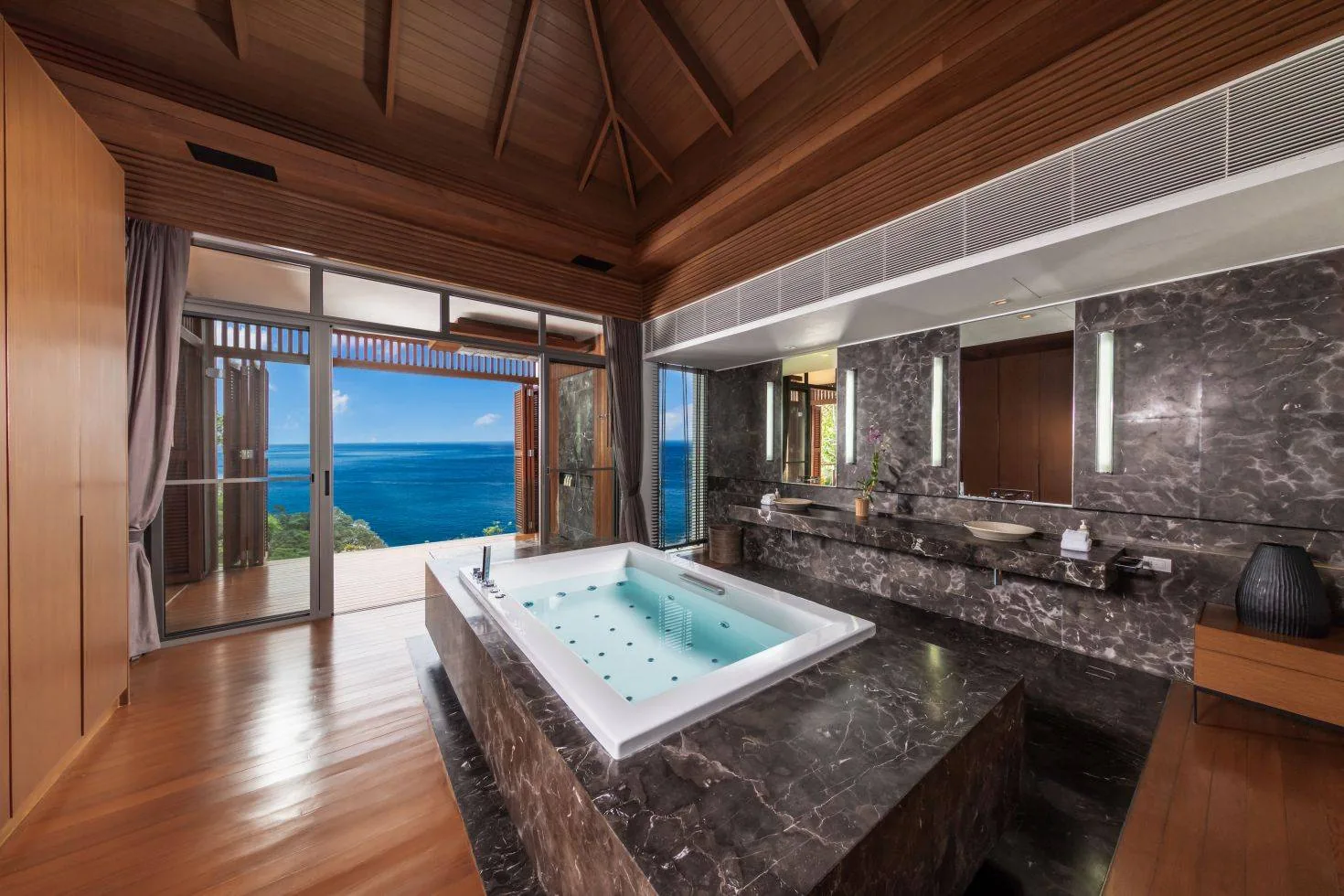A bathroom with a dark stone clad tub and a view of the sea through the window