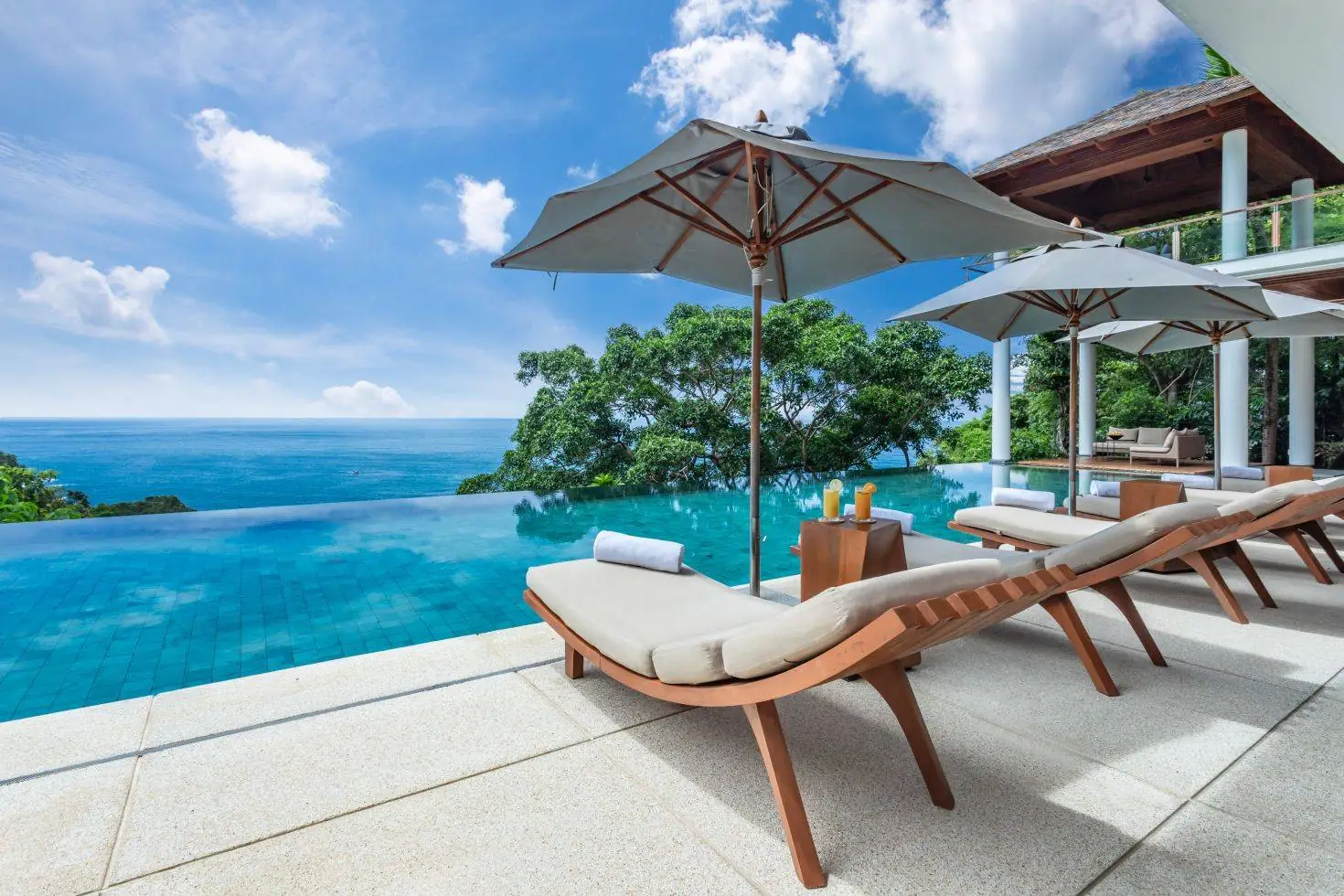 Teak sun loungers and umbrellas on the travertine pool terrace above the Andaman Sea