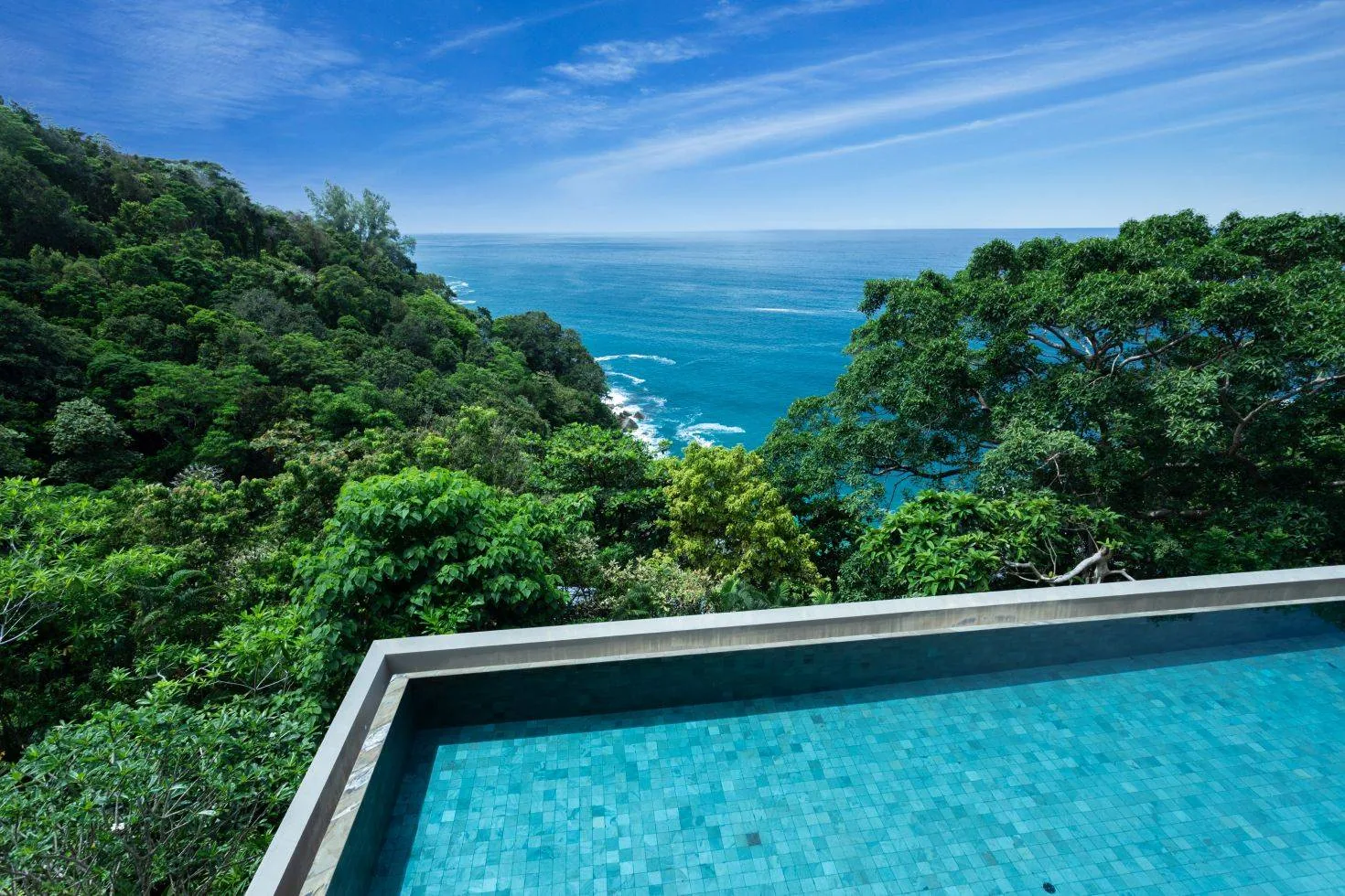 An elevated view of the pool with the sea and forested coastline beyond