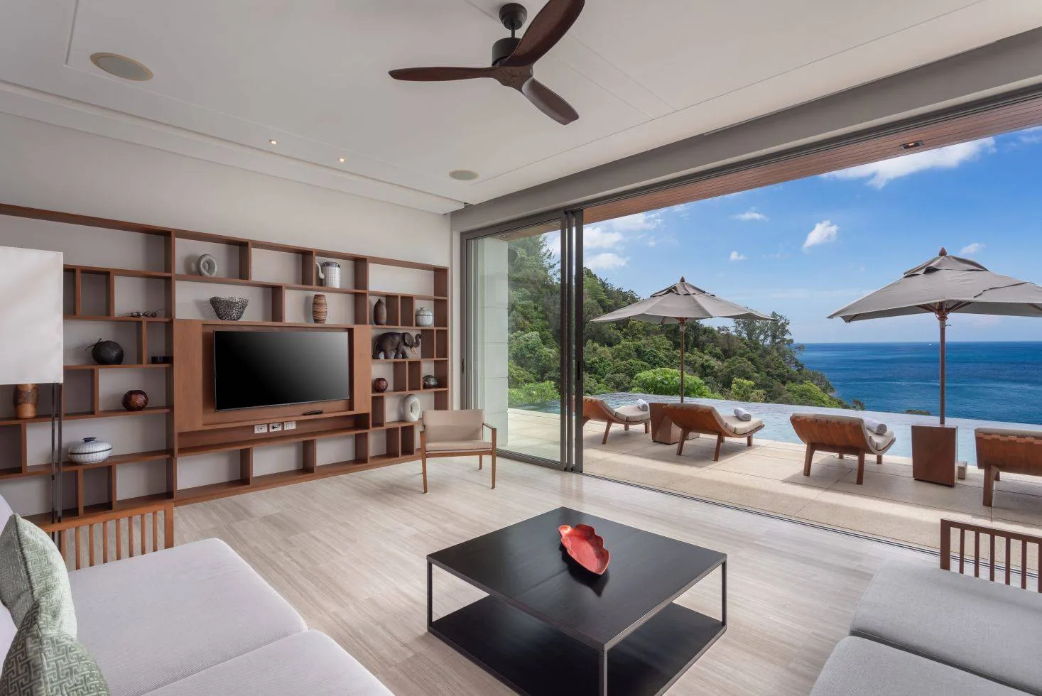 A living room open to a terrace with loungers and the sea beyond