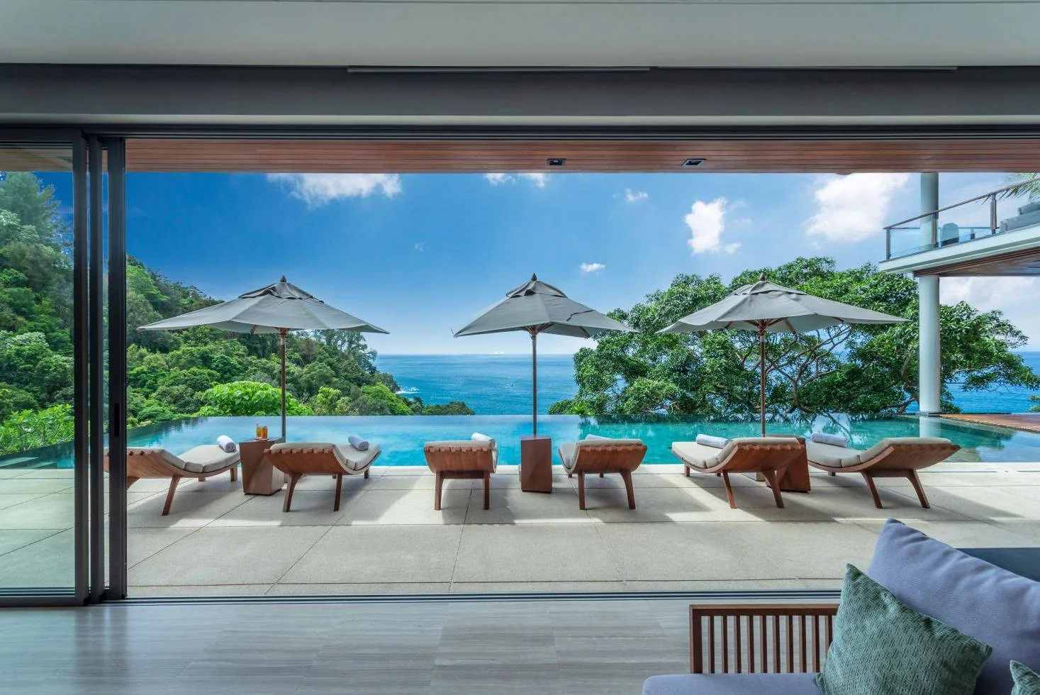 Sun loungers under umbrellas beside the pool, seen from inside the villa, with a sea view